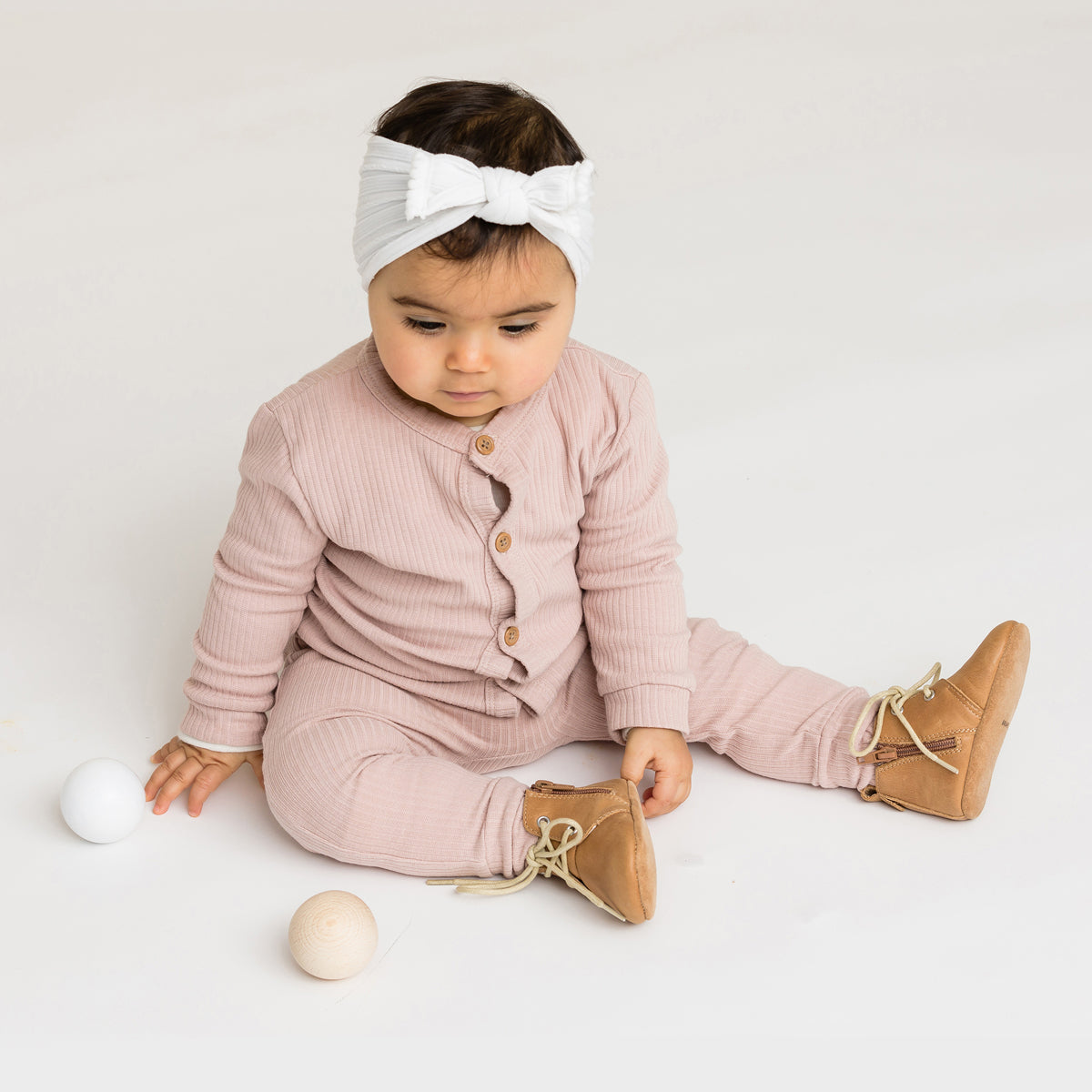 Toddler wearing Tan boots with white laces with white bow in hair